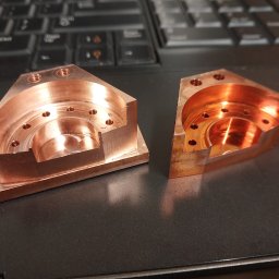 Edgecut Łukasz Chudzik - Dwie precyzyjnie obrobione, miedziane części z otworami, leżące na laptopie. Widoczne ślady obróbki skrawaniem i detale wykonania.
