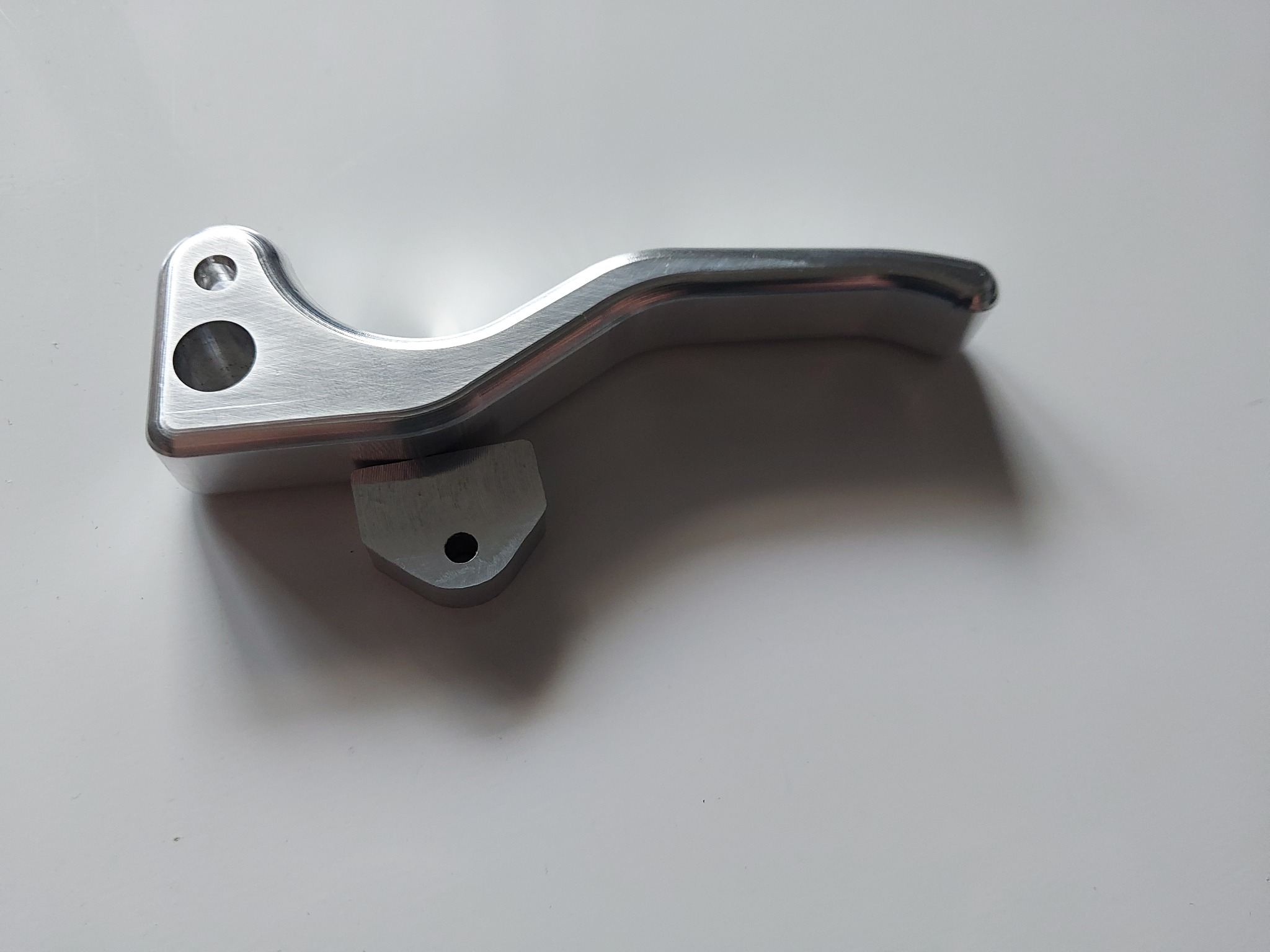 Precyzyjnie obrobiony, metalowy element z widocznymi otworami i gładką powierzchnią, leżący na jasnym tle. Detal wykonany z dbałością o szczegóły.