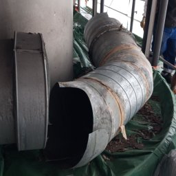 Profesjonalne usługi rozbiórek ręcznych Michał K. - Fragmenty metalowych rur wentylacyjnych na zielonej folii budowlanej, pozostałości po demontażu instalacji wewnątrz budynku. Widoczne elementy konstrukcji stropu.