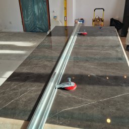 InStyle - Ciemna, marmurkowa płyta na stole z narzędziem do cięcia płytek Rubi Slim Cutter Plus. W tle poziomica i drzwi zabezpieczone folią.