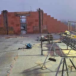 AMJ Michał Jezierski - Budowa domu w trakcie realizacji: mur z pustaków Porotherm, zbrojenie na rusztowaniu, narzędzia budowlane, mgła w tle. Widok z góry na plac budowy.