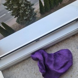 Czysty Dom-Usługi Sprzątające - Fioletowa ściereczka leży na marmurowym parapecie okna z widokiem na drzewa i ulicę. Okno jest białe, a ściereczka ma strukturę wafla.