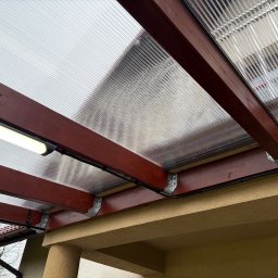 UNOVIA - Zadaszenie tarasu z poliwęglanu, drewniana konstrukcja w kolorze mahoniu, oświetlenie LED. Widok z dołu, detale mocowań i instalacji elektrycznej.