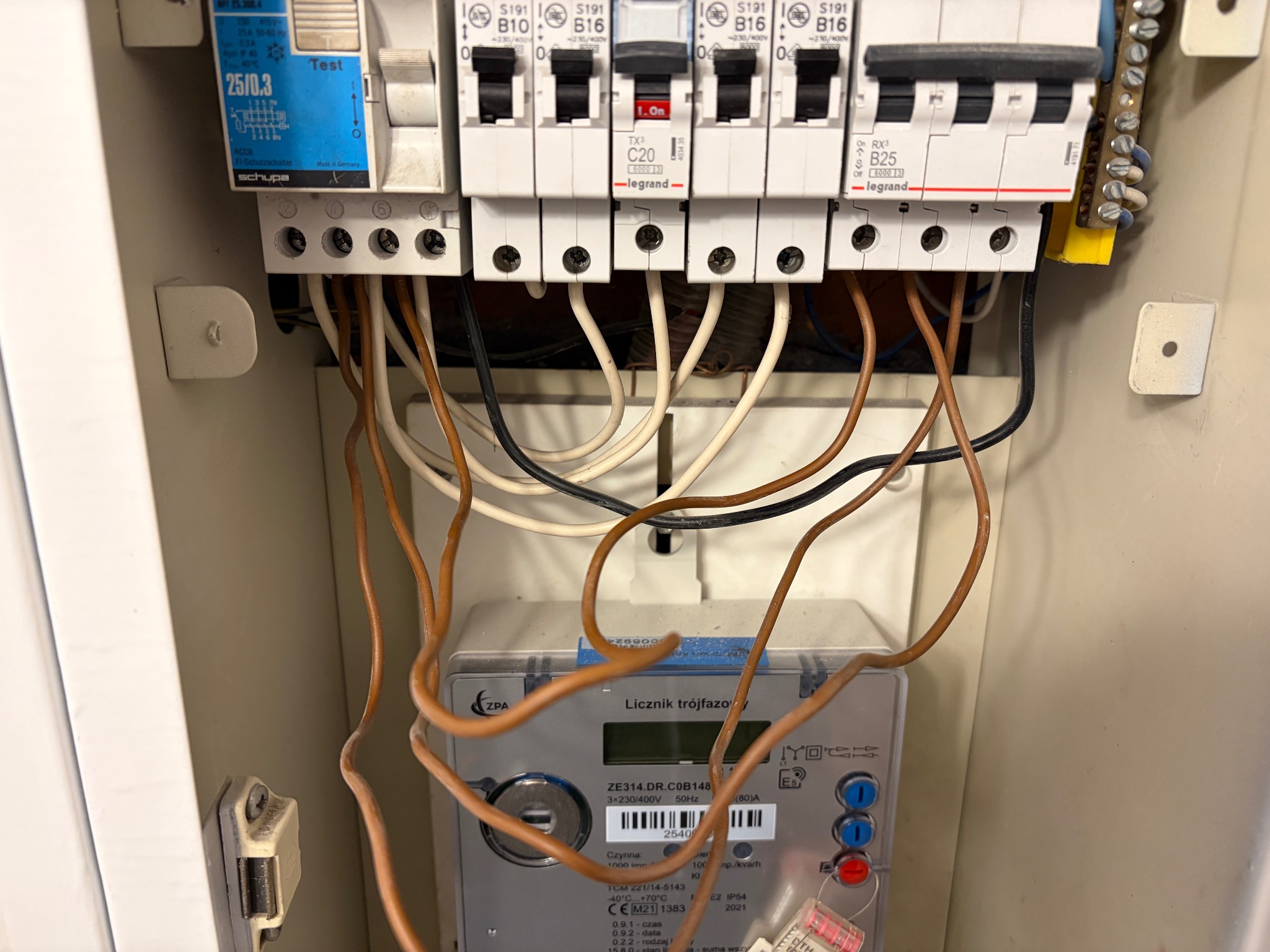 Rozdzielnia elektryczna z licznikiem trójfazowym ZPA, bezpiecznikami Legrand i przewodami wewnątrz obudowy. Widoczne elementy instalacji elektrycznej.