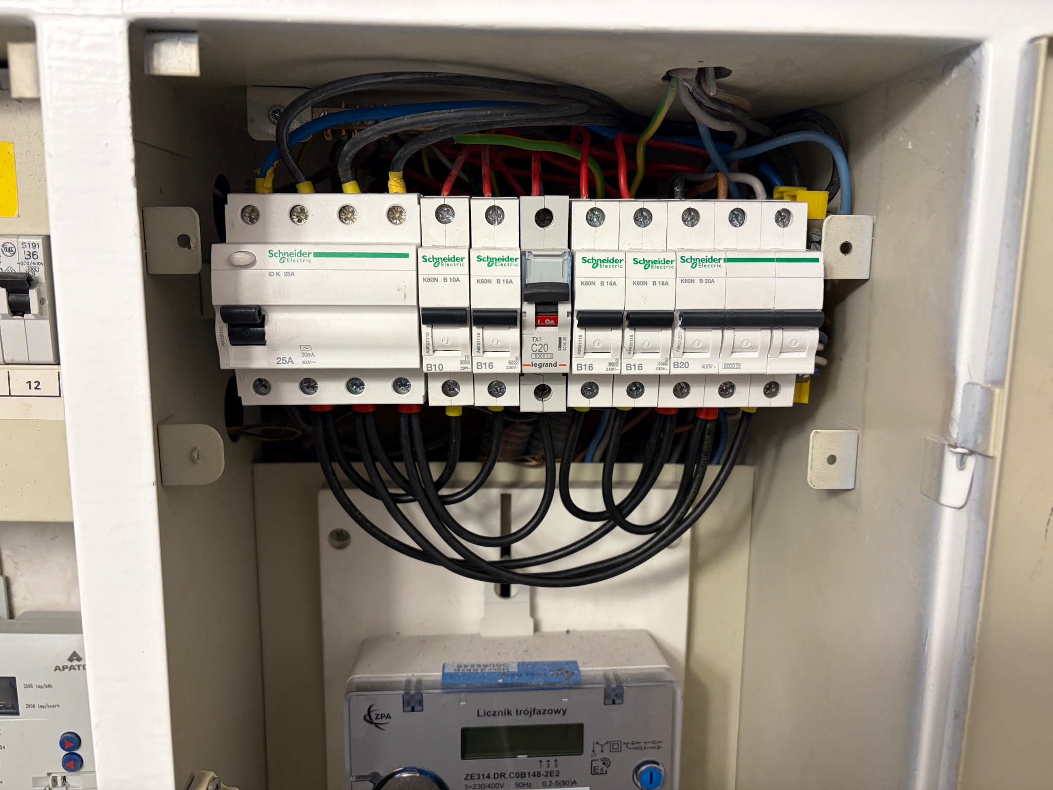 Rozdzielnia elektryczna z zainstalowanymi bezpiecznikami Schneider i licznikiem trójfazowym ZPA. Widoczne przewody i elementy instalacji wewnątrz skrzynki.