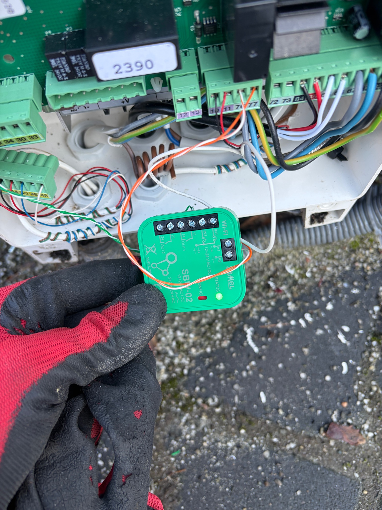 Podłączenie modułu Wi-Fi SBW-02 do sterownika bramy. Widoczne złącza, przewody i ręka w roboczej rękawicy. Integracja inteligentnego sterowania bramą.