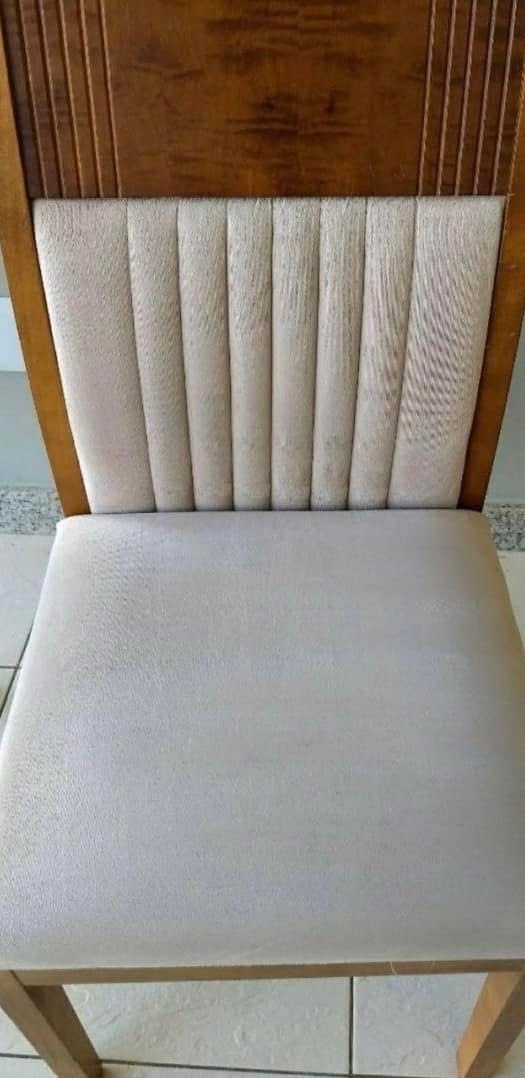 Tapicerowane krzesło z drewnianym oparciem, widoczne z przodu. Jasna tapicerka siedziska i oparcia z pionowymi przeszyciami. Widoczne ślady użytkowania na siedzisku.