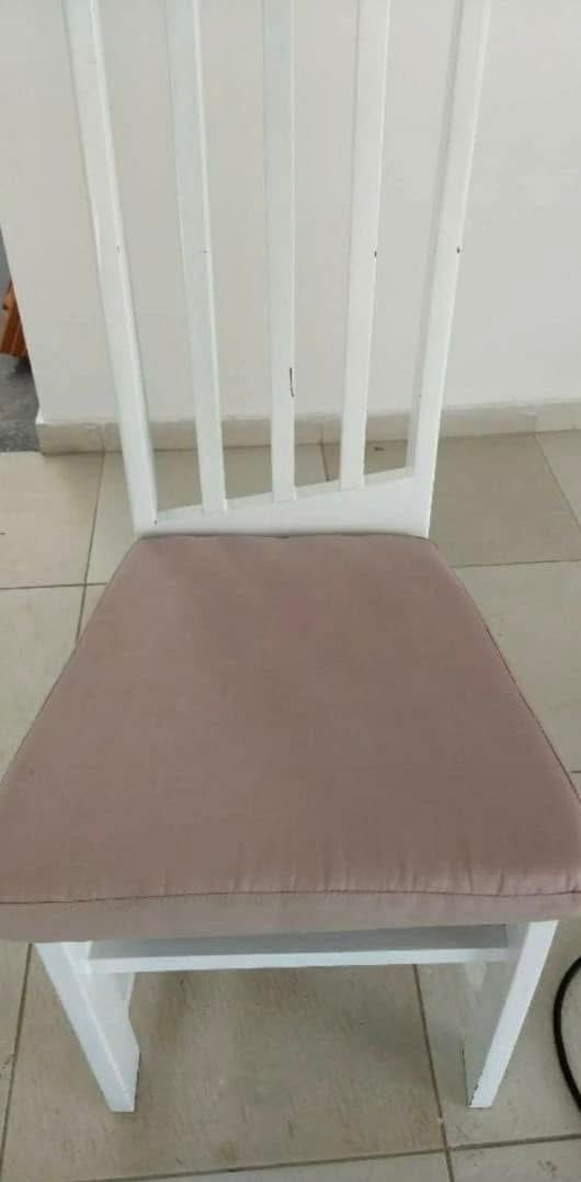 Białe krzesło z tapicerowanym siedziskiem w odcieniu pudrowego różu, ustawione na kafelkach. Widok z przodu, skupiony na siedzisku i oparciu krzesła.