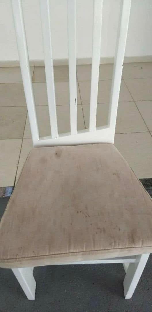 Białe krzesło z beżowym, zabrudzonym siedziskiem na tle jasnej podłogi. Widoczne plamy na tapicerce. Krzesło ustawione przodem do obiektywu.