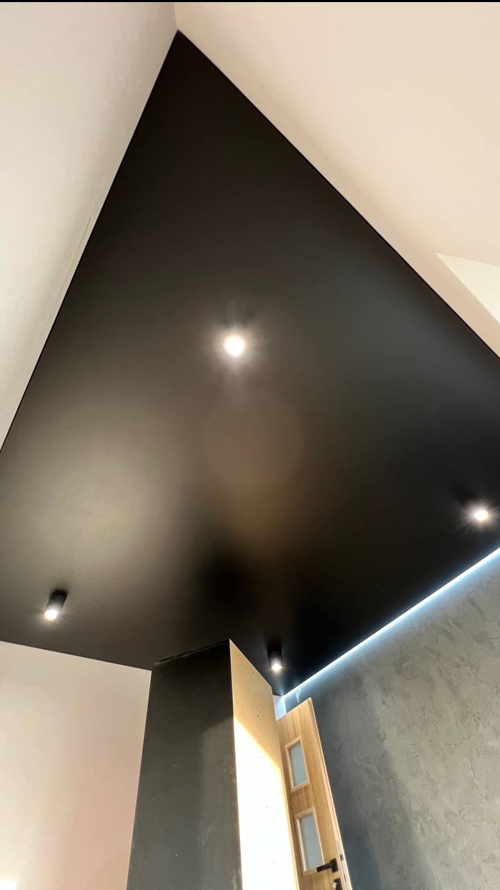 Czarny, matowy sufit napinany z oświetleniem punktowym i listwą LED w Gdyni. Nowoczesny design, widok z dołu, fragment drzwi. Minimalistyczne wykończenie wnętrza.