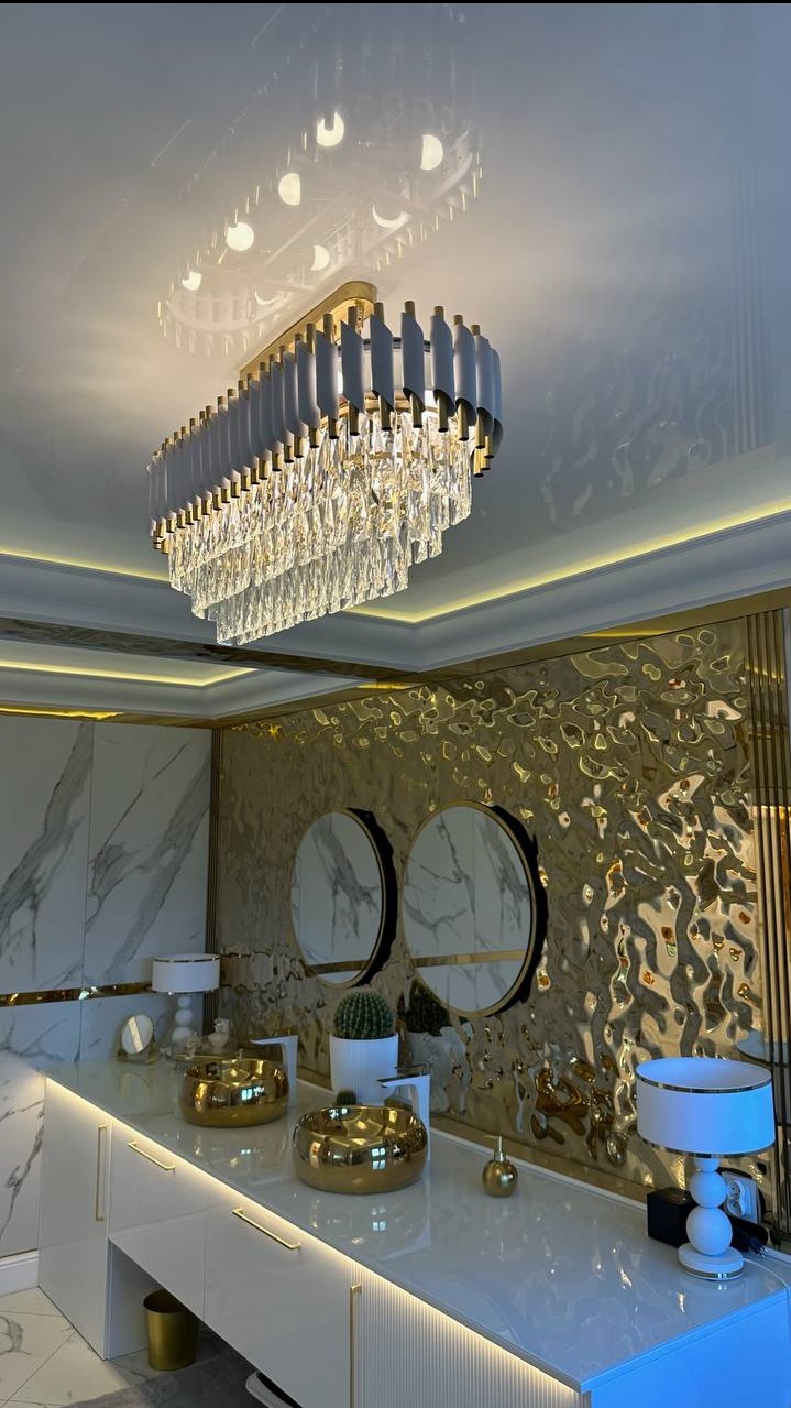 Elegancki sufit napinany z kryształowym żyrandolem, złote akcenty na ścianie i meblach, marmurowe elementy, oświetlenie LED, nowoczesny design.