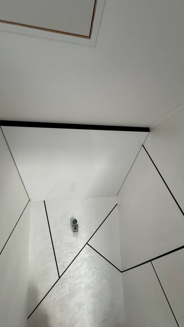 Biały sufit napinany z czarnymi akcentami w nowoczesnej łazience. Widoczny właz rewizyjny i minimalistyczna lampa. Geometryczny wzór na ścianach.