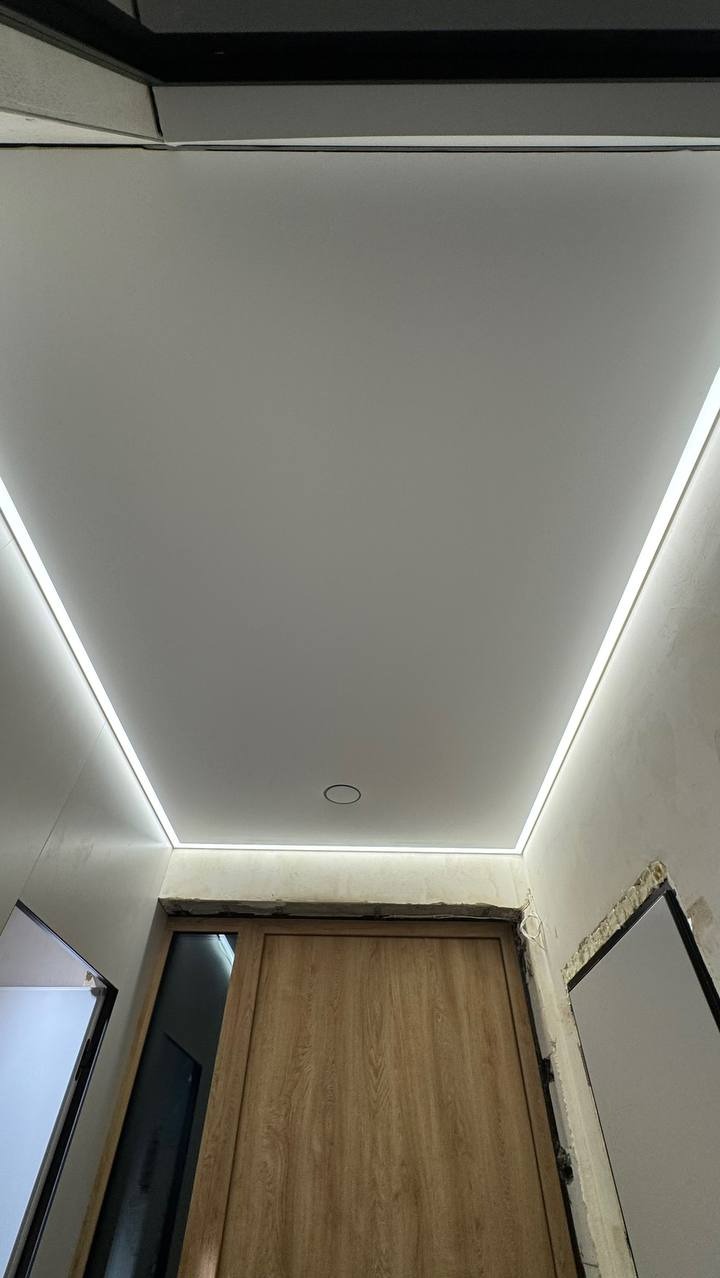 Biały sufit napinany z oświetleniem LED, widok z dołu na drewniane drzwi. Minimalistyczny design, nowoczesne wykończenie wnętrza.