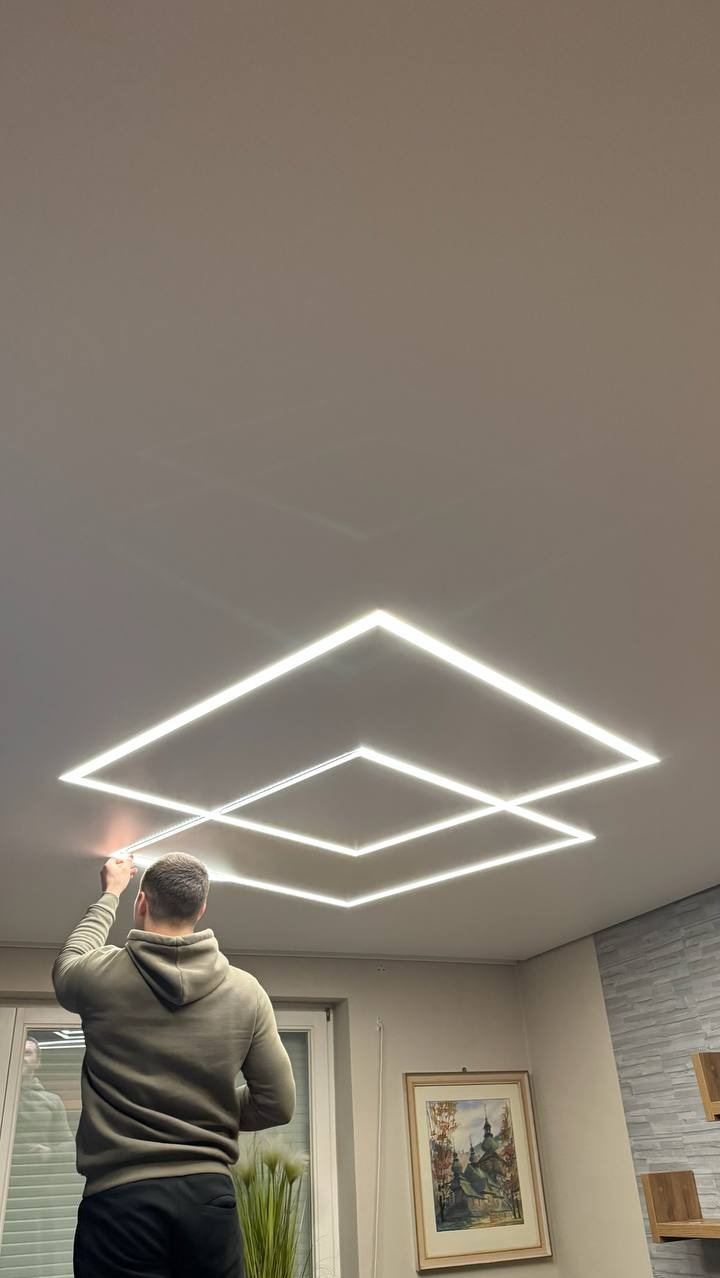 Montaż sufitu napinanego z oświetleniem LED w kształcie kwadratów. Widoczna osoba podczas instalacji, jasne światło, neutralne tło. Nowoczesny design.