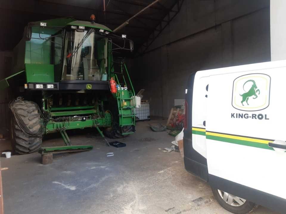 Zielony kombajn John Deere w hali, częściowo zasłonięty przez biały samochód dostawczy z logo King-Rol. Widoczne narzędzia i akcesoria serwisowe.