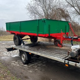 Tomasz Simlat - Laweta z zielono-czerwoną przyczepą na platformie, widok z boku, szara pogoda, teren podmokły. Przyczepa zabezpieczona pasami, widoczna wciągarka.