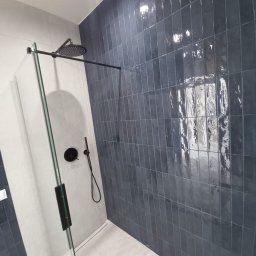 71INSIDE - Nowoczesna kabina prysznicowa z grafitowymi, błyszczącymi płytkami ułożonymi pionowo, czarna armatura i szklana ściana. Minimalistyczny design, jasna podłoga.