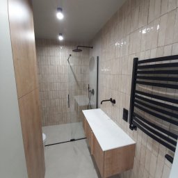 71INSIDE - Nowoczesna łazienka z kabiną typu walk-in, beżowymi płytkami imitującymi cegłę, drewnianą szafką pod umywalką i czarnym grzejnikiem drabinkowym.