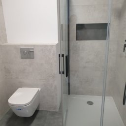 71INSIDE - Nowoczesna łazienka po remoncie: kabina prysznicowa z czarnymi detalami, podwieszana toaleta i płytki imitujące kamień. Minimalistyczny design z wnęką w ścianie.