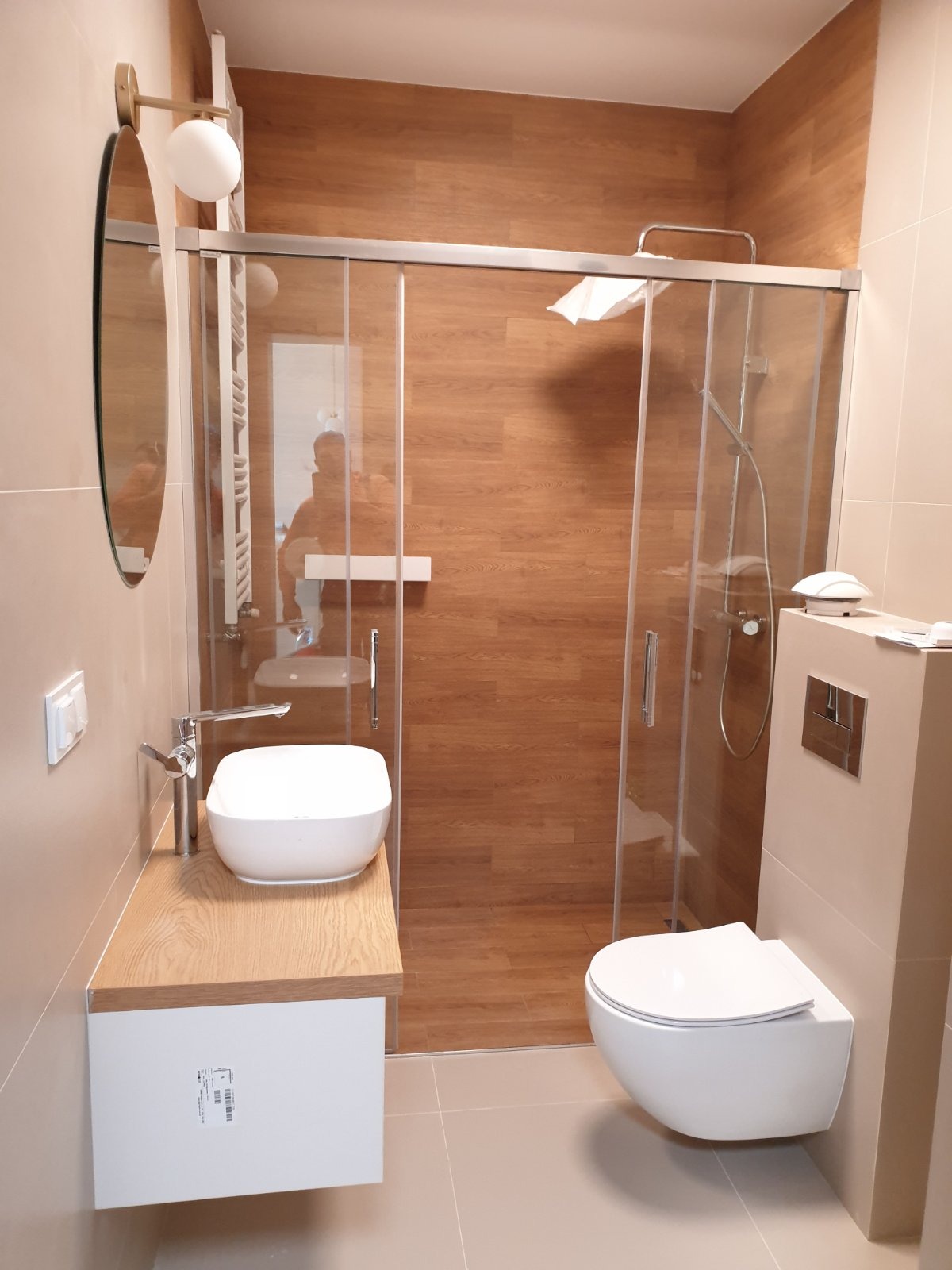 Nowoczesna łazienka z kabiną prysznicową typu walk-in, umywalką nablatową na drewnianym blacie i podwieszaną toaletą. Ściany wykończone płytkami imitującymi drewno.
