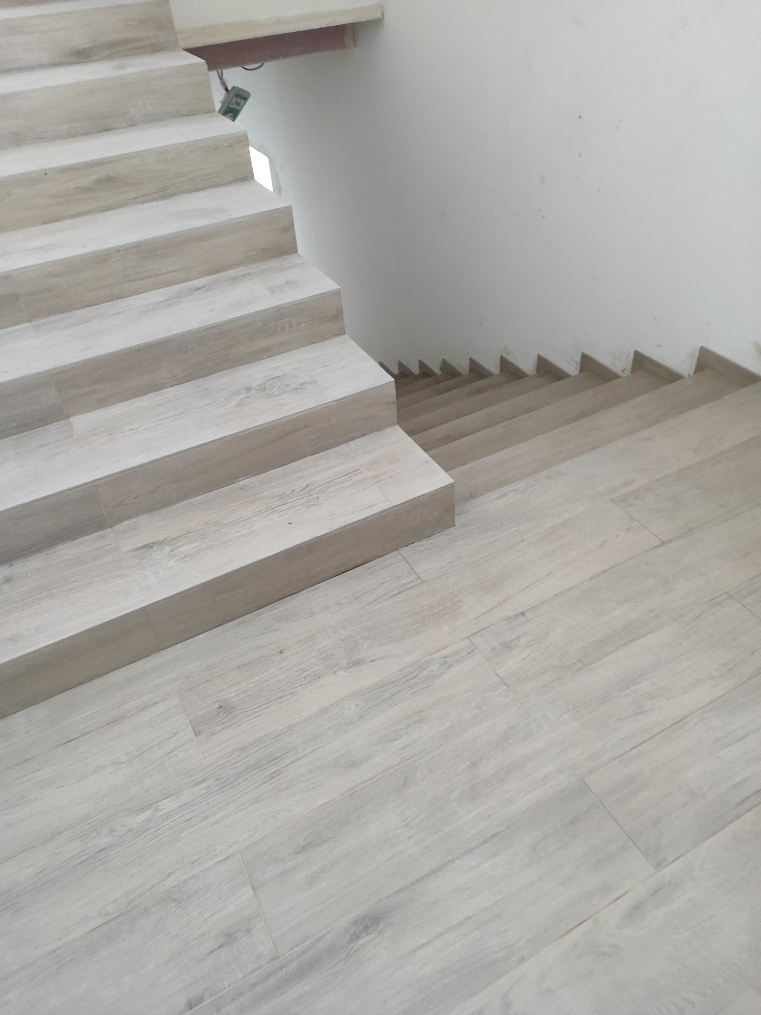 Jasne, drewnopodobne płytki na schodach i podłodze, ułożone w regularny wzór. Minimalistyczne wykończenie wnętrza, widok z góry na fragment schodów i podłogi.