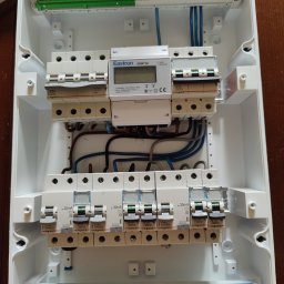 Jarosław Gołembiewski - Rozdzielnica elektryczna w białej obudowie z zainstalowanymi bezpiecznikami, licznikiem energii i okablowaniem. Widoczne elementy marki Legrand i Eastron.