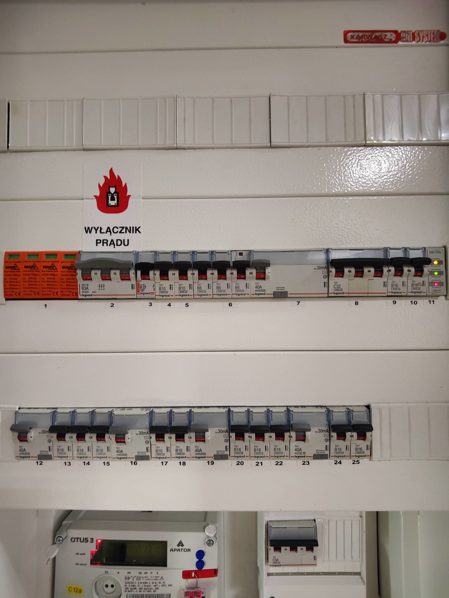 Rozdzielnia elektryczna z bezpiecznikami, licznikiem i oznaczeniem 'Wyłącznik Prądu'. Widoczne elementy instalacji elektrycznej wewnątrz obudowy.