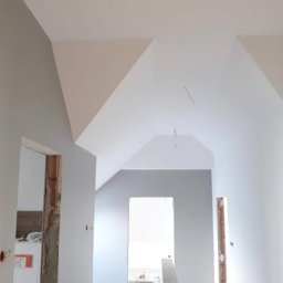 Ekspresowe Metamorfozy - Wnętrze po malowaniu: szare ściany kontrastują z białym sufitem w skosach. Widoczne ościeżnice drzwiowe w trakcie wykończenia. Minimalistyczny design, jasne kolory.