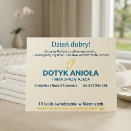 Dotyk Anioła - Karta firmy sprzątającej 'Dotyk Anioła' na tle posłanego łóżka i stosu ręczników, obok czekoladka. Akcent na czystość i komfort w ofercie.