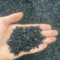 Skład Handlowy ADAMIX Adam Skrobosiński - Dłoń trzymająca w zagłębieniu dłoni miał węglowy na tle hałdy miału. Widoczne drobne, czarne frakcje węgla. Dłoń lekko zabrudzona pyłem.