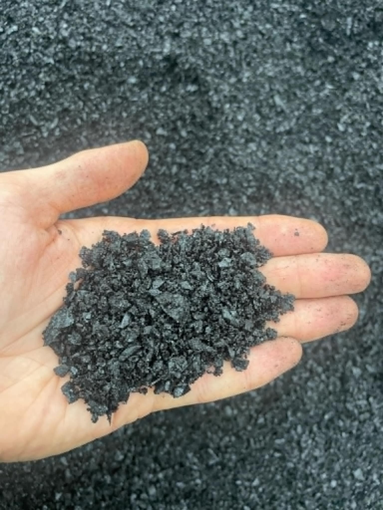 Dłoń trzymająca w zagłębieniu dłoni miał węglowy na tle hałdy miału. Widoczne drobne, czarne frakcje węgla. Dłoń lekko zabrudzona pyłem.