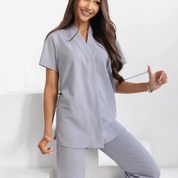 Veronica Medina - Uśmiechnięta brunetka prezentuje szary komplet: spodnie i bluzę z krótkim rękawem, stojąc na białych schodach. Ubranie z kieszeniami, z gumką do regulacji.