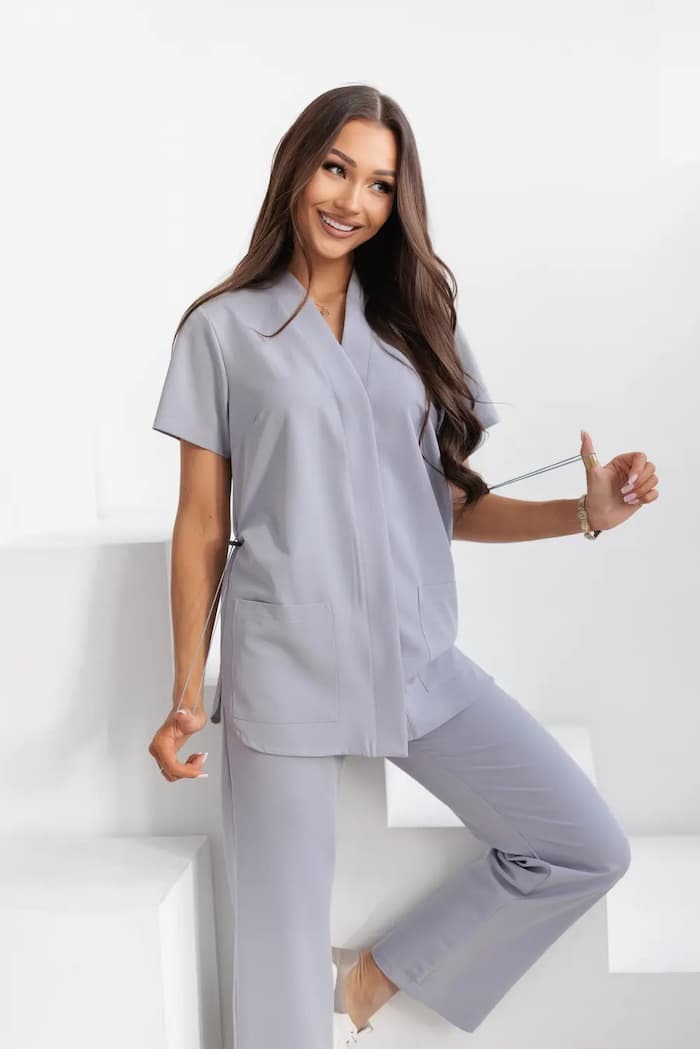 Uśmiechnięta brunetka prezentuje szary komplet: spodnie i bluzę z krótkim rękawem, stojąc na białych schodach. Ubranie z kieszeniami, z gumką do regulacji.