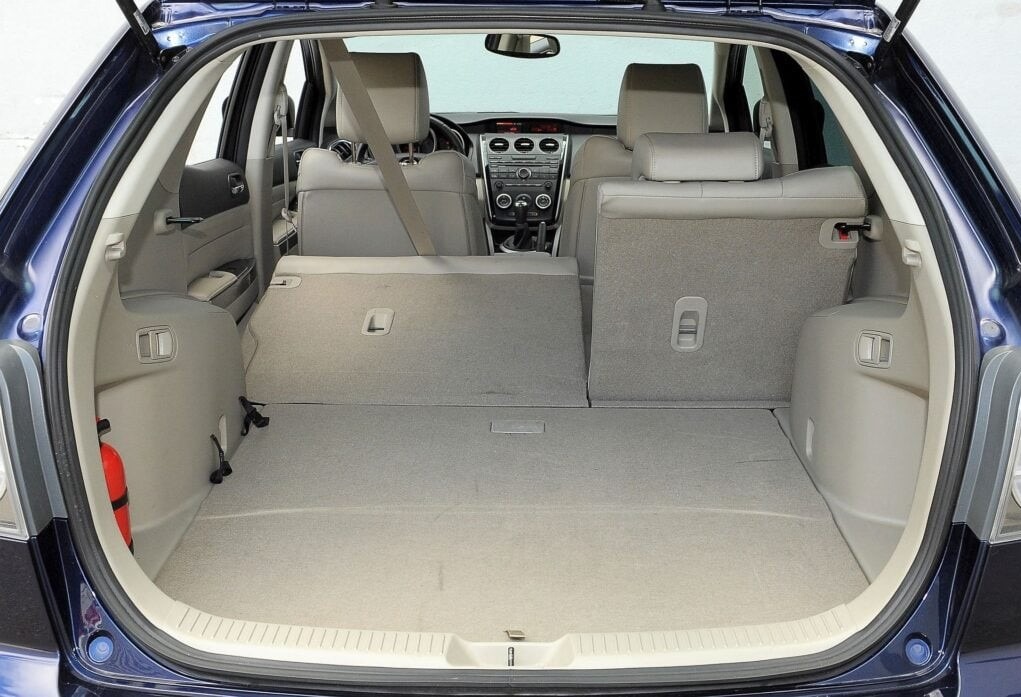 Bagażnik niebieskiego samochodu typu kombi z widocznymi siedzeniami i deską rozdzielczą. Przestrzeń bagażowa pusta, gotowa do załadunku. Widoczna gaśnica.