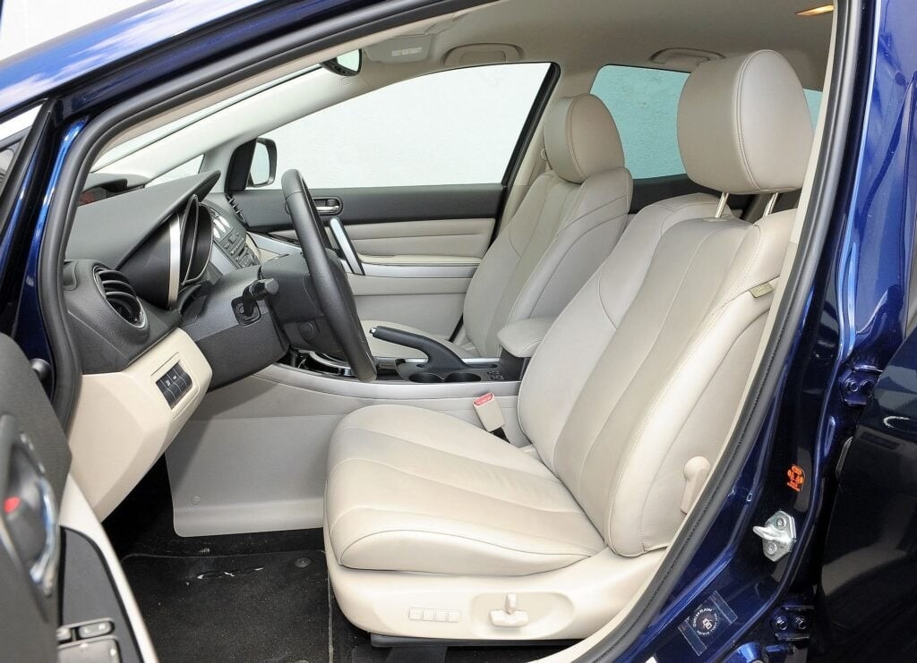 Wnętrze niebieskiego samochodu z jasną, skórzaną tapicerką. Widoczne przednie fotele, deska rozdzielcza i kierownica. Czyste i zadbane wnętrze pojazdu.