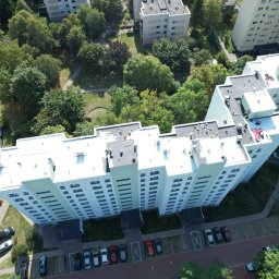 TOSIEZATEGUJE.PL SPÓŁKA Z OGRANICZONĄ ODPOWIEDZIALNOŚCIĄ - Z lotu ptaka: ekipa na jasnym dachu wysokiego bloku, prawdopodobnie podczas prac remontowych. Widoczne drzewa, parking i inne budynki w tle.