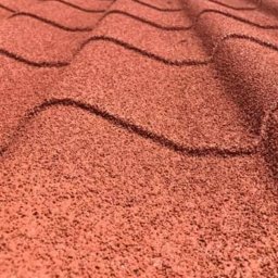 TOSIEZATEGUJE.PL SPÓŁKA Z OGRANICZONĄ ODPOWIEDZIALNOŚCIĄ - Czerwona dachówka bitumiczna w zbliżeniu, ukazująca teksturę i falisty wzór. Widoczne delikatne cieniowanie podkreśla trójwymiarowość pokrycia dachowego.