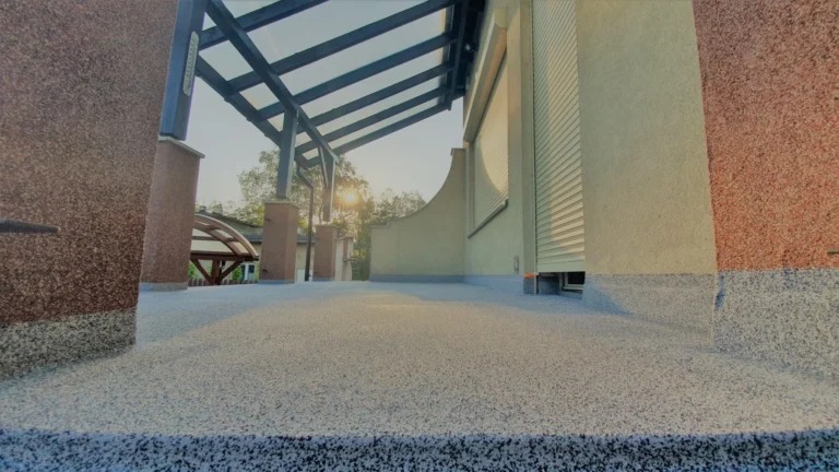 Wykończony taras z żywicy w Krakowie, zadaszony pergolą i roletami zewnętrznymi. Widok z niskiej perspektywy podkreśla strukturę powierzchni i detale wykończenia elewacji.