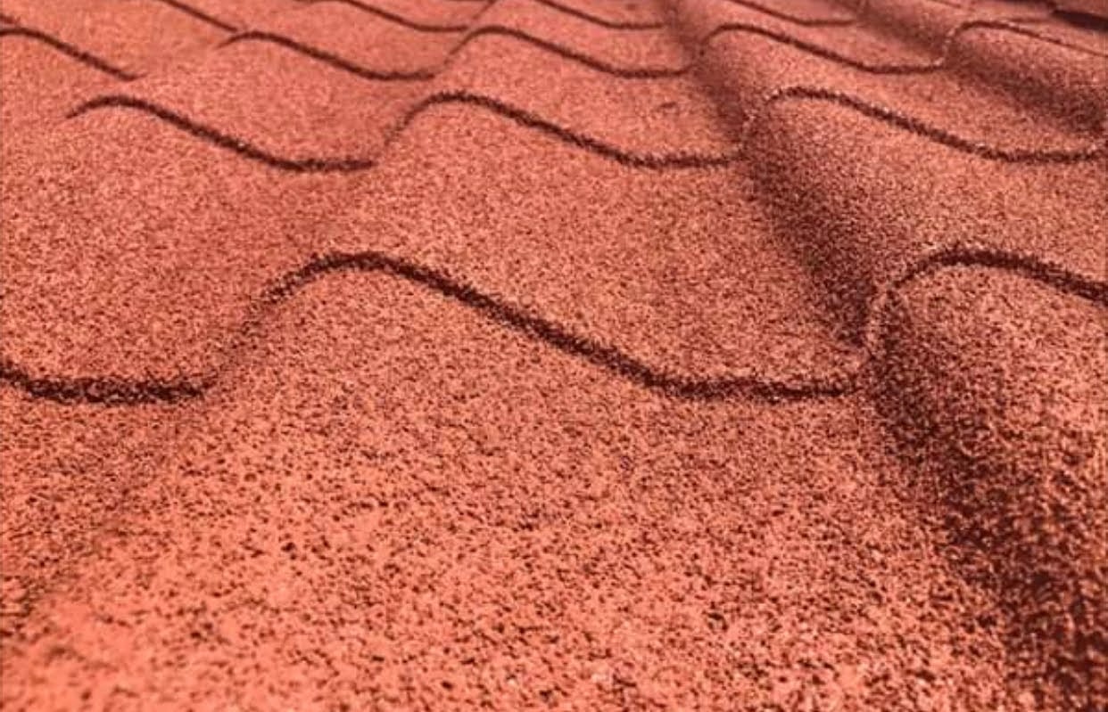 Czerwona dachówka bitumiczna w zbliżeniu, ukazująca teksturę i falisty wzór. Widoczne delikatne cieniowanie podkreśla trójwymiarowość pokrycia dachowego.