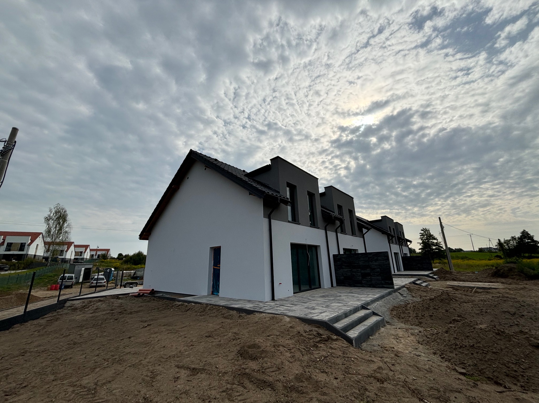 Nowoczesne szeregówki z kostką brukową na tarasie i schodach, teren przygotowany pod ogród, pochmurne niebo. Widok z dołu.