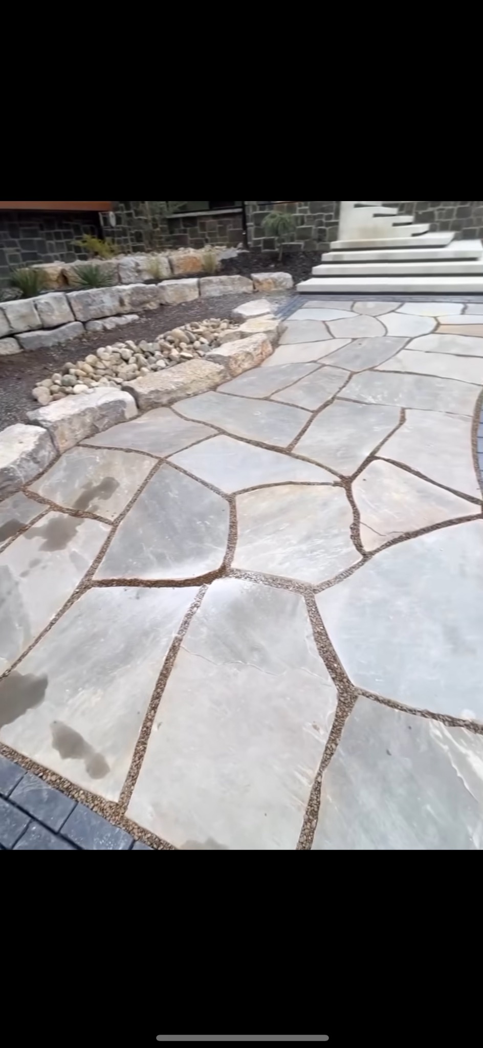 Ścieżka z nieregularnych płyt kamiennych z drobnym żwirem w spoinach, prowadząca do schodów i skalniaka. Kamienne obrzeża rabat.