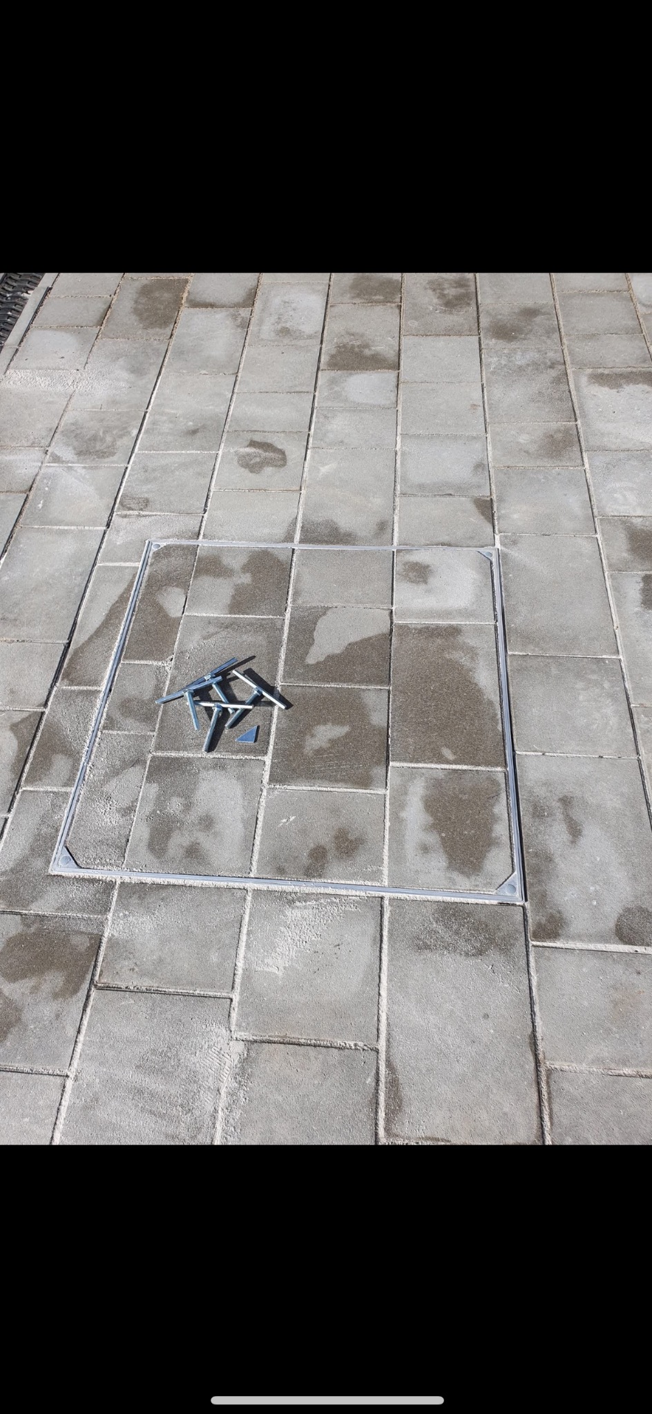 Szara kostka brukowa z metalową ramą i narzędziami do układania. Widok z góry, oświetlenie dzienne, detale fug i faktury kostki.