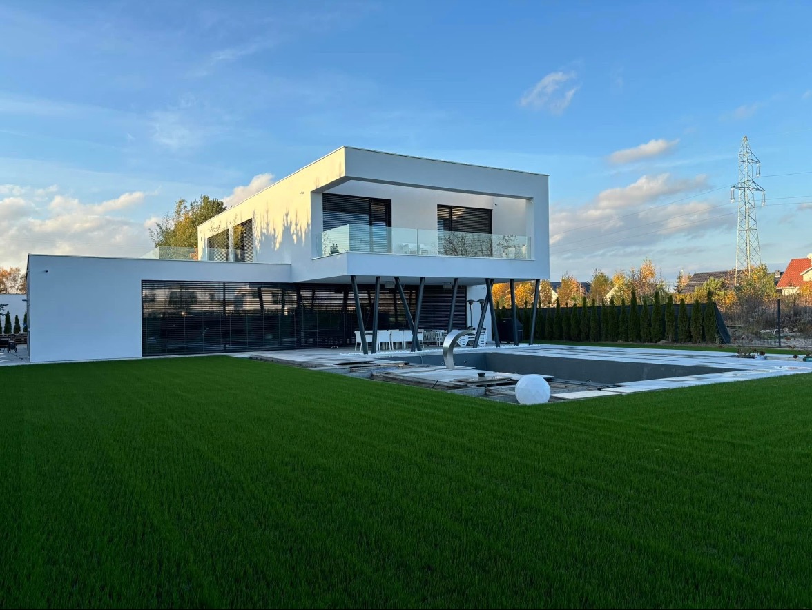 Nowoczesny dom z basenem i równo przystrzyżonym trawnikiem w słoneczny dzień. Minimalistyczna architektura, szklane balustrady i geometryczne kształty.