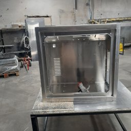 MaxPol - Spawana, metalowa obudowa urządzenia na stole warsztatowym. Widoczne ślady obróbki, spawania. W tle elementy warsztatu i składowane blachy.