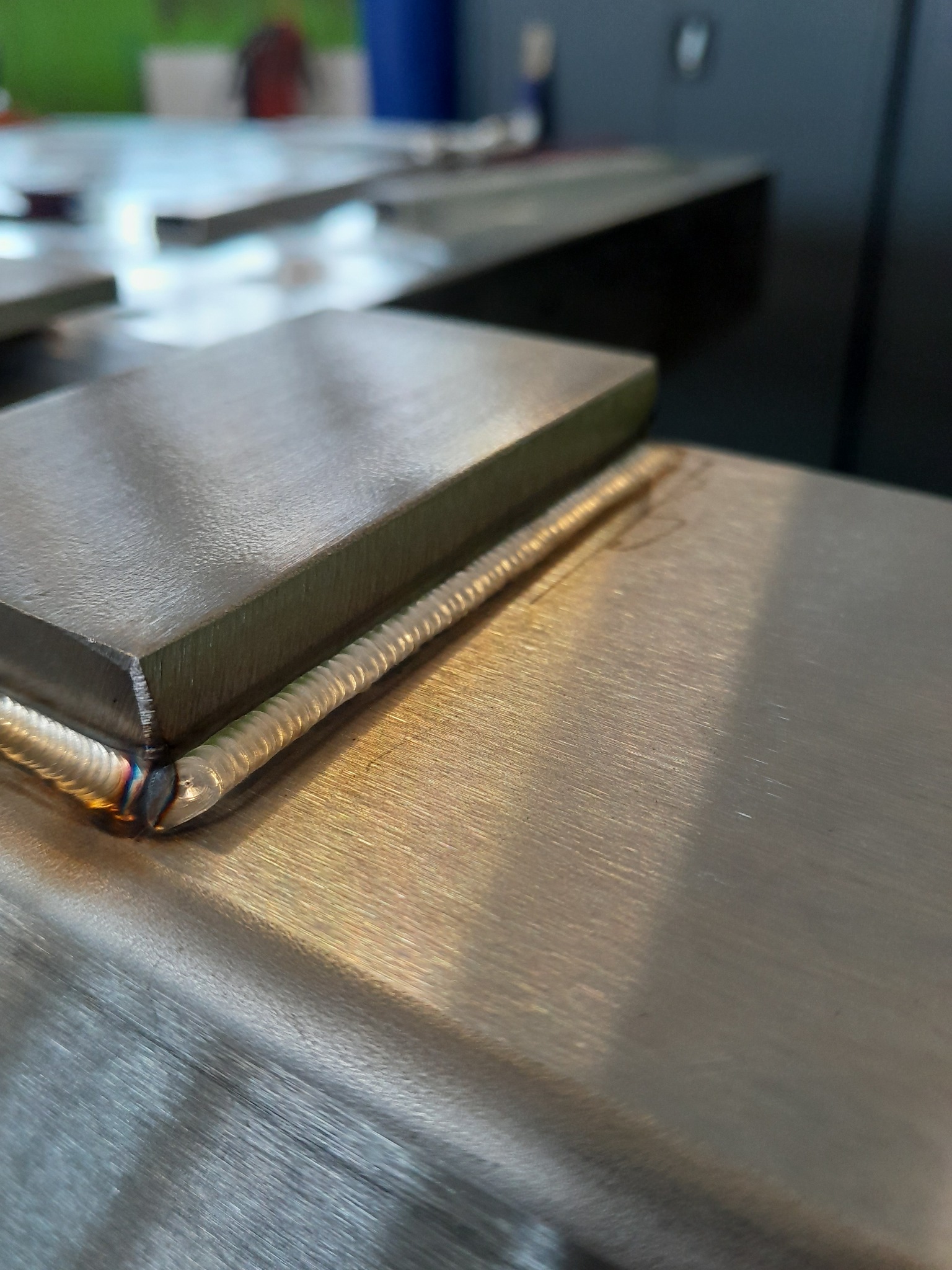 Precyzyjne łączenie metalowych elementów widoczne z bliska, ukazujące estetyczne spawy na powierzchni obrabianego metalu. Detal spoiny z efektem tęczy.