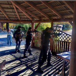 IVAN-OLEKSANDR Yakymiv Centrum Szkoleń - Szkolenie strzeleckie: grupa osób w czarnych strojach ćwiczy celowanie z broni pod drewnianą wiatą, z widoczną osobą obserwującą w tle.