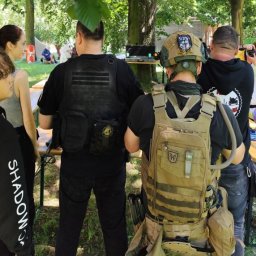 IVAN-OLEKSANDR Yakymiv Centrum Szkoleń - Uczestnicy w taktycznych kamizelkach i hełmach podczas plenerowej imprezy integracyjnej. Widoczny fragment stołu i drzewa w tle.