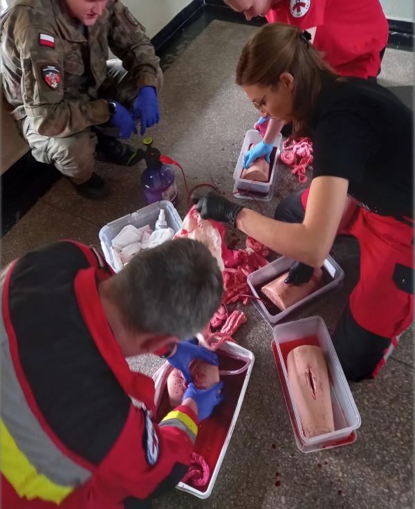 Symulacja ran podczas kursu pierwszej pomocy: instruktorzy i kursanci ćwiczą na fantomach, używając sztucznej krwi i rekwizytów imitujących obrażenia.