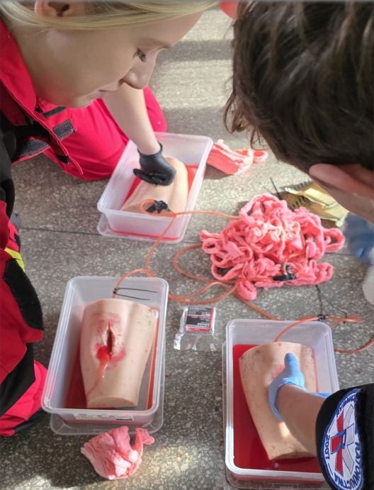 Kurs pierwszej pomocy: Instruktorzy demonstrują opatrywanie ran na manekinach z symulacją krwawienia podczas szkolenia z zakresu ratownictwa medycznego.