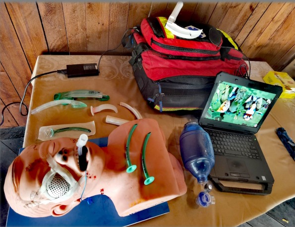 Manekin do nauki RKO z rurkami intubacyjnymi, workiem ambu i laptopem z prezentacją, na stole z drewnianym tłem. Sprzęt do kursu pierwszej pomocy.